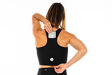 Model placing phone in back pocket of Black Core Crop. Women's running top with pockets.