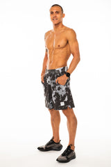 Left view model wearing Arvo Shorts with hands in pockets. Camo running shorts with reflective logo on left thigh.