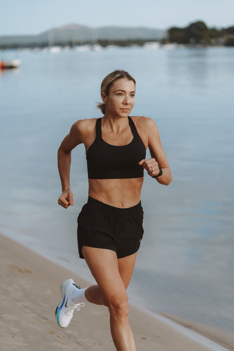 Model running along the beach in the black all sport support high impact bra.