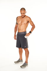 Model placing a phone in the side pocket of his Arvo Shorts. Men's grey gym shorts with pockets.