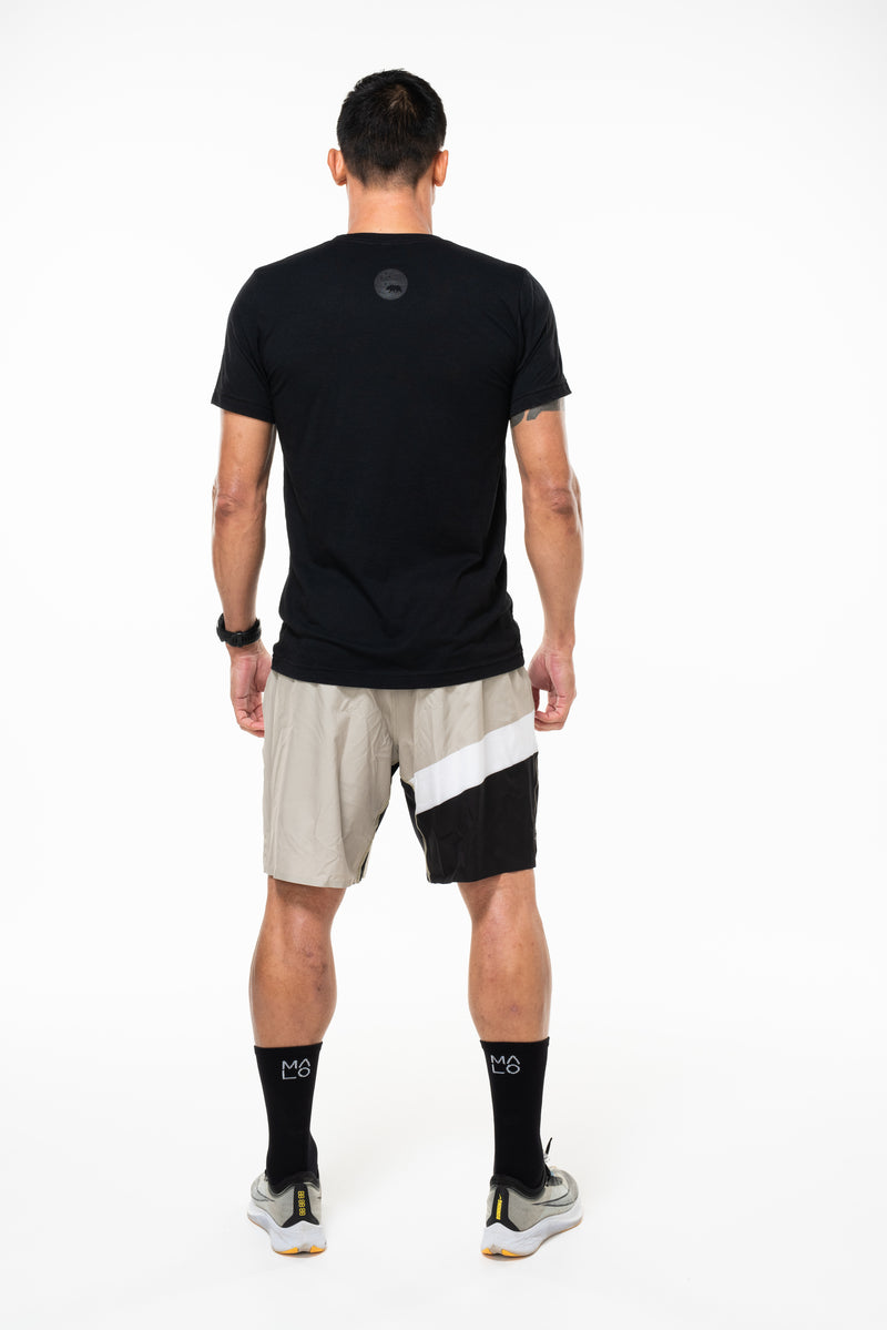 Back view of sand/black Arvo Shorts. Tan workout shorts with reflective logo on waistline.