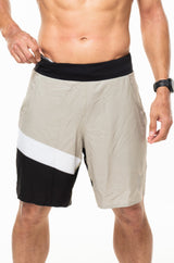 Model placing keys in small waistline pocket of Arvo Shorts. Light brown running shorts with pockets.