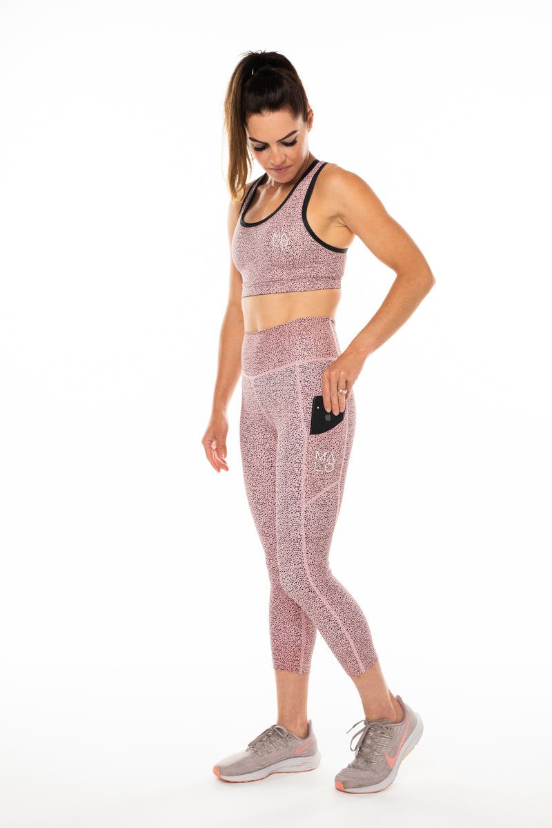 Model placing a phone in side pocket of left leg in pink 3/4 leggings.