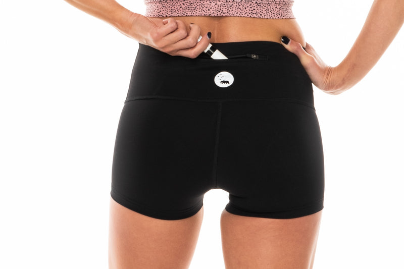 Model placing keys in back pocket of PR Shorts. Black workout shorts with zipper pocket in waistband.