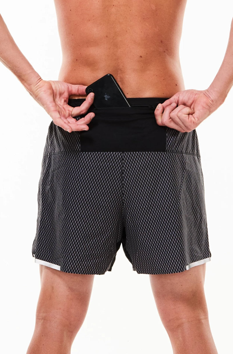 Model placing phone in back pocket of Black Reflect Noosa Run Short. Lined running shorts with pockets